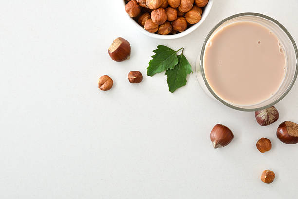 Glass of hazelnut drink isolated on white table with bowl of peeled and shelled nuts and leaves around. Top view.