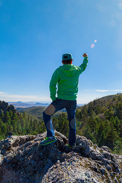 Young adult hiker stands triumphantly on a rocky peak, overlooking the lush landscape of peñas cargadas, hidalgo