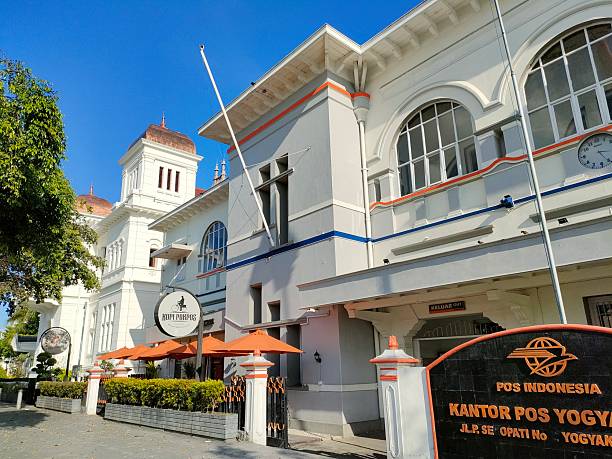 Yogyakarta, Indonesia -  April, 2025 :   the iconic Kantor Pos Yogyakarta (Yogyakarta Main Post Office), a colonial-style building located on Jalan Panembahan Senopati. The structure stands out with its white facade, large arched windows, and a clock mounted on the upper wall. In front of the building, there's a café called 