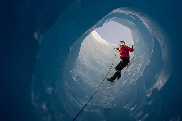 Female explorer climbing a rope within a breathtaking blue ice cave, surrounded by stunning glacier formations and pristine wilderness
