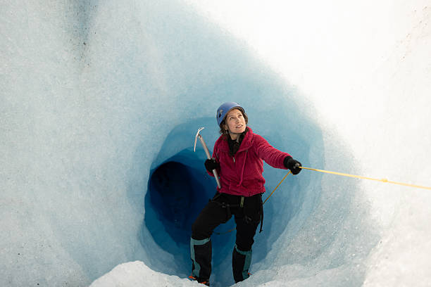 Female glaciologist exploring a deep glacial crevasse with ice axe and rope