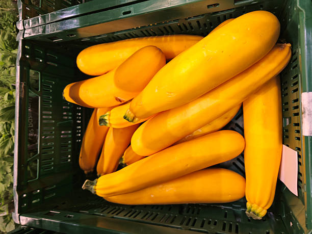 Bright yellow zucchinis neatly stacked in a green plastic crate at a market stall. The bold contrast between the vivid yellow vegetables and the green container highlights freshness and seasonal abundance, perfect for promoting healthy eating and plant-based diets.