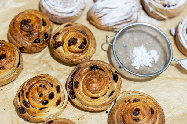 istock Freshly baked raisin and cinnamon rolls with sifter, top view 2213143443