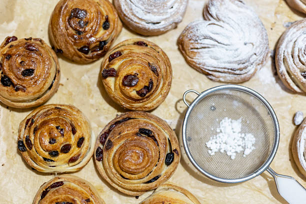 istock Freshly baked cinnamon raisin rolls displayed on parchment paper with a sifter used for adding powdered sugar. Perfectly golden, these pastries are tempting and ready to serve. 2213143494