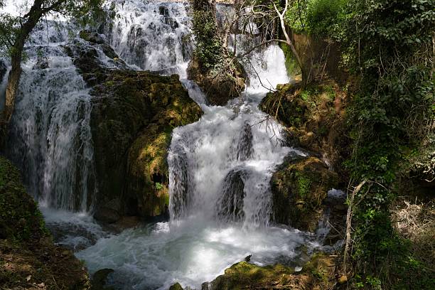 istock Serene waterfall cascading over mossy rocks in a lush forest setting during bright daylight 2213154865