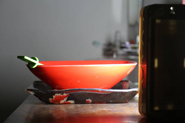 A red bowl with green spoon is placed on a black tray decorated with floral patterns, and both items are situated on a wooden surface.