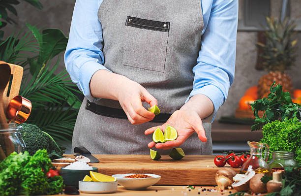 istock Cooking food in the kitchen. Chef holds sliced lime. Wooden table, kitchenware, vegetables, herbs and ingredients. Healthy vegan eating, recipes, blogging 2213160550