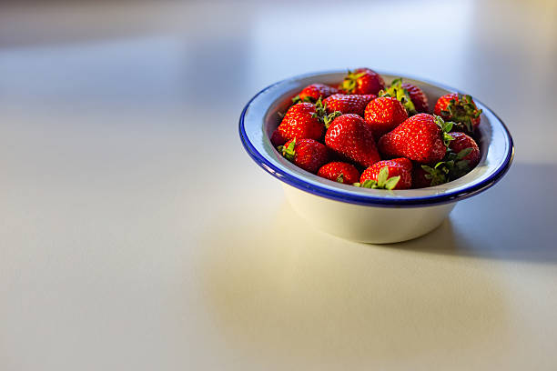 Madrid. Spain. Ripe, juicy strawberries are piled high in an enamel bowl with a blue rim, sitting on a clean white table, ready to be enjoyed