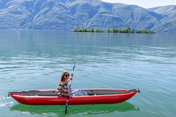 Woman paddling a red kayak on calm waters, serene mountain backdrop. Adventurer enjoying an outdoor experience. Scenic nature setting for water sports enthusiasts.