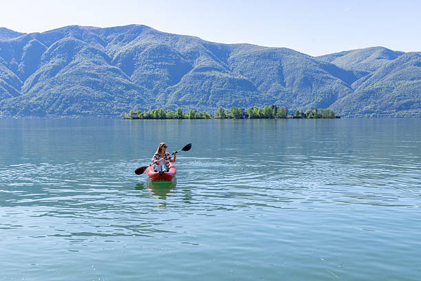 Woman paddles red kayak on clear mountain lake. Adventurous solo travel in nature. Scenic outdoor activity on tranquil waters.