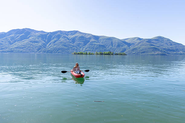 Woman paddles red kayak on clear mountain lake. Adventurous solo travel in nature. Scenic outdoor activity on tranquil waters.