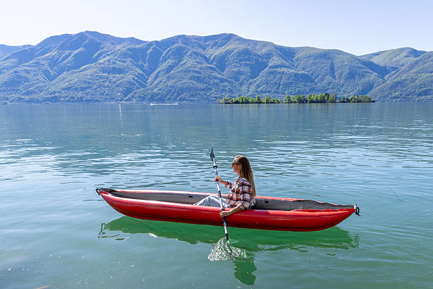 Woman paddling in a red kayak across peaceful lake with mountains in background. Solo adventure seeker kayaking on calm water. Scenic outdoor exploration in nature.