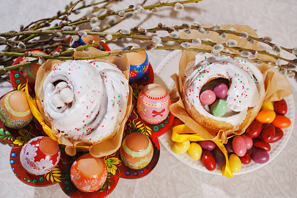 Colorful decorated eggs are arranged alongside sweet pastries topped with icing and sprinkles. Fresh branches add a festive touch to this vibrant spring gathering featuring traditional treats.