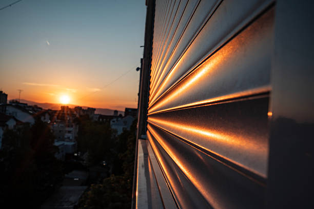 Warm sunset light reflects off a textured metallic surface with a scenic city view. The composition highlights the contrasting interplay of natural light and urban geometry, creating a visually compelling perspective.