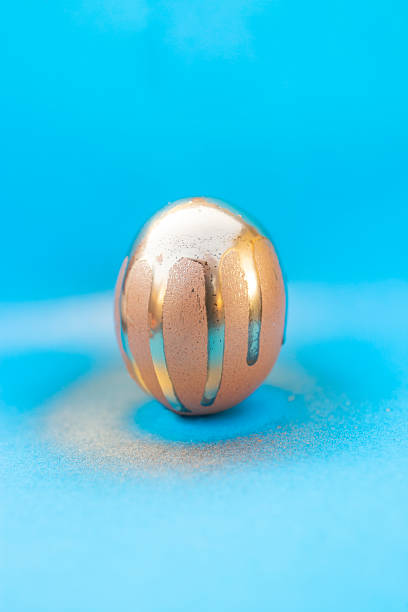 istock Golden spray paint trails on a chicken egg on blue background 2213171708