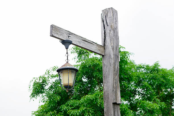 A rustic wooden post supports a vintage lantern, illuminating a serene outdoor space. Lush green foliage adds charm and tranquility to the setting.