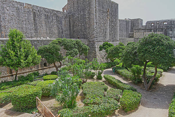 Dubrovnik, Croatia - June 13, 2010: Green Garden Park in Front of Stone Walls Fortress at Sunny Summer Day.