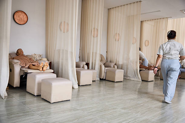Relaxing spa environment featuring individuals in comfortable chairs, separated by light curtains, receiving treatments. The setting is calm and inviting, emphasizing rest, self-care, and rejuvenation in a tranquil atmosphere.