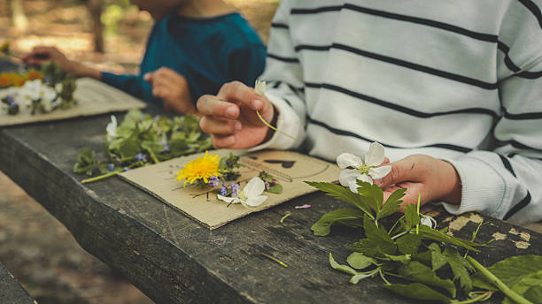 istock Children creating handmade flower crafts using cardboard, drawing vases and attaching real spring blossoms. Creative outdoor activity on a rustic wooden table in the forest 2213188069
