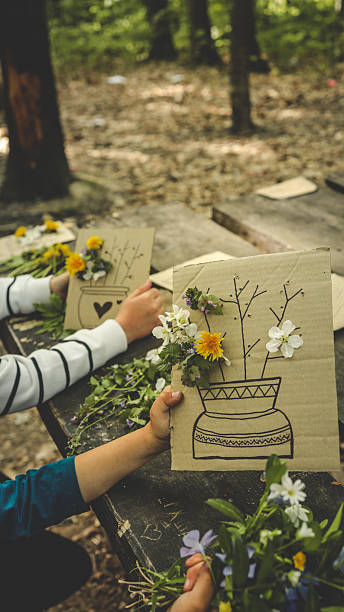 istock Children creating handmade flower crafts using cardboard, drawing vases and attaching real spring blossoms. Creative outdoor activity on a rustic wooden table in the forest 2213188079