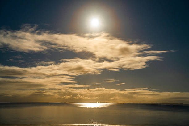 Moon in the clouds of the night sky over the water surface of the sea in Browns Bay