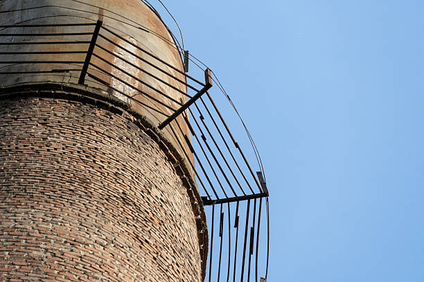A low-angle view of a towering brick structure with a rusty metal railing, set against a cloudless blue sky.