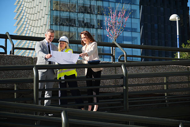 Architects and engineers reviewing blueprints in front of modern buildings
