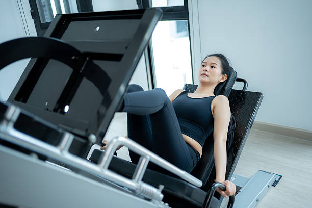 Asian woman training on leg press machine at gym.