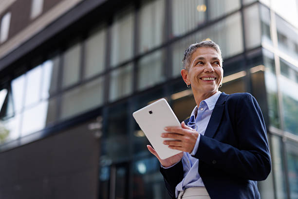 istock Happy mature businesswoman using digital tablet while standing outside modern office building 2213213045