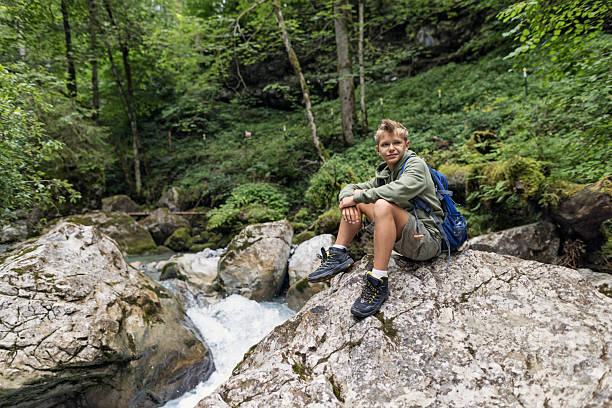 Teenage hiker resting on a boulder by a forest stream