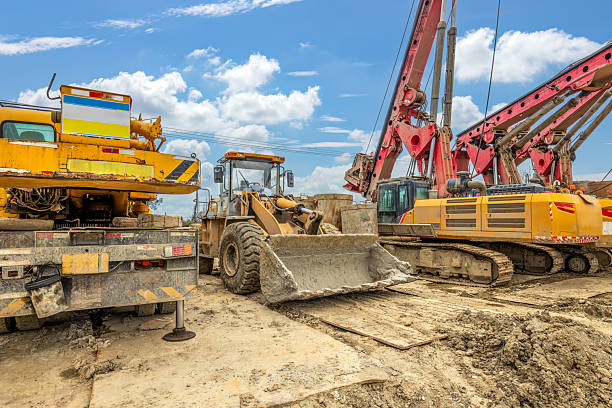 Heavy construction machinery includes yellow loader vehicle and red drilling rig at outdoor work site.
