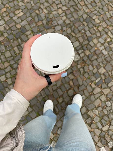 Woman wearing smart ring while holding coffee cup walking on cobblestone street