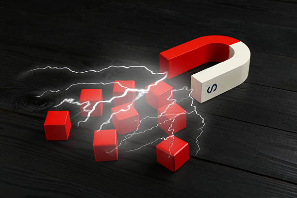 Magnet with lightnings attracting red cubes on black wooden table