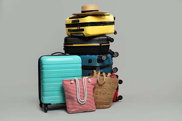 istock Stack of colorful suitcases, beach bags and straw hat on grey background 2213223269