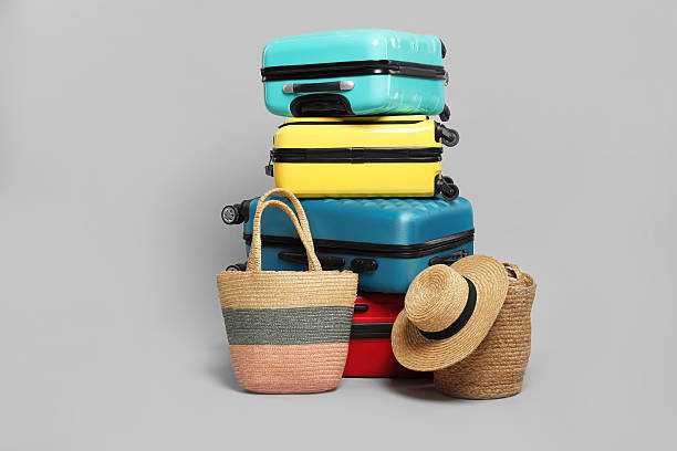 istock Stack of colorful suitcases, beach bags and straw hat on grey background 2213223295