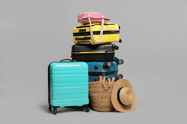istock Stack of colorful suitcases, beach bags and straw hat on grey background 2213223360