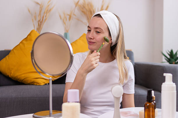 istock Young woman using jade roller massaging face skin at home looking in the mirror 2213232246