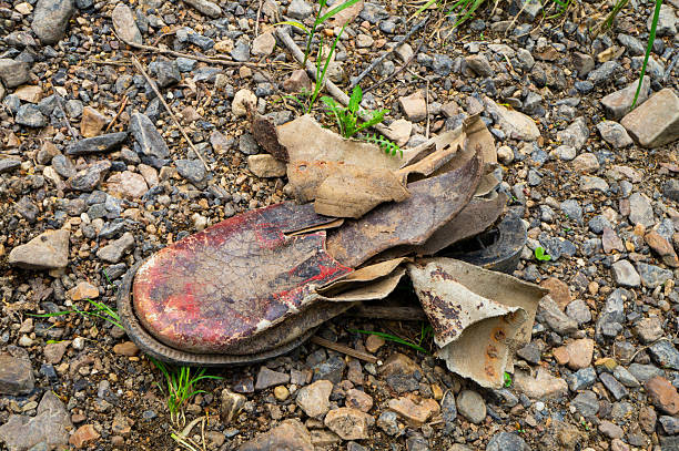 istock Old worn leather boots among stones on the river bank. Interesting texture close-up. 2213235286