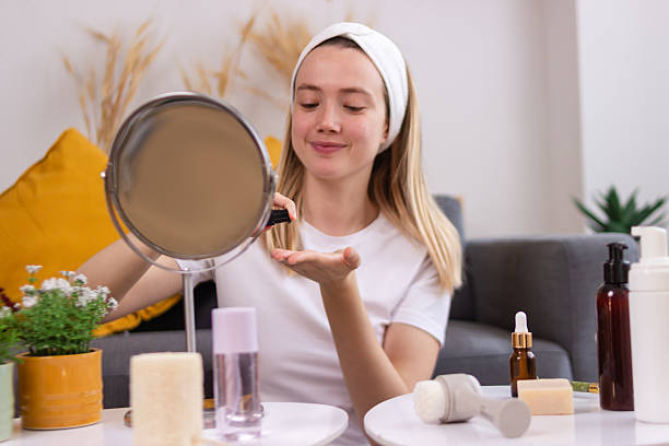 istock Young woman applying moisturizer on face while looking in mirror at home 2213236995