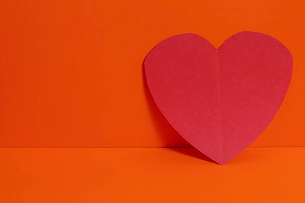 A red paper heart nestled on a vibrant orange background for Valentine's Day and Mother's Day.