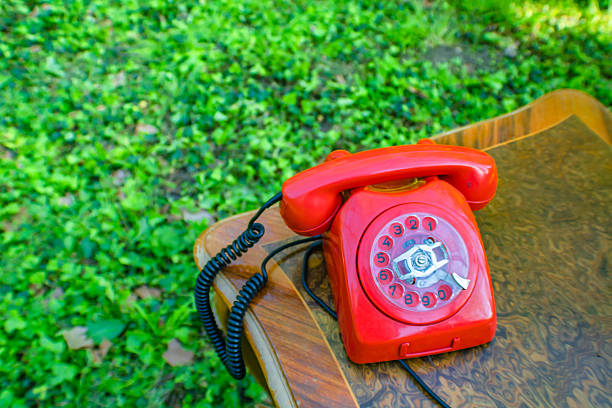 A vintage red, rotary dial telephone on a brown table, green grass background