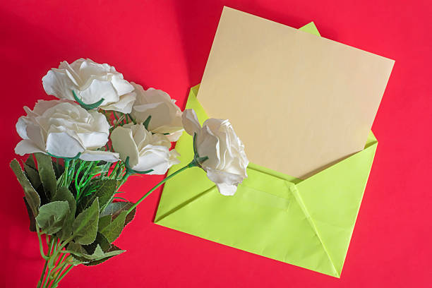 A beautiful arrangement of delicate white roses next to a vibrant green envelope on a bright red surface.