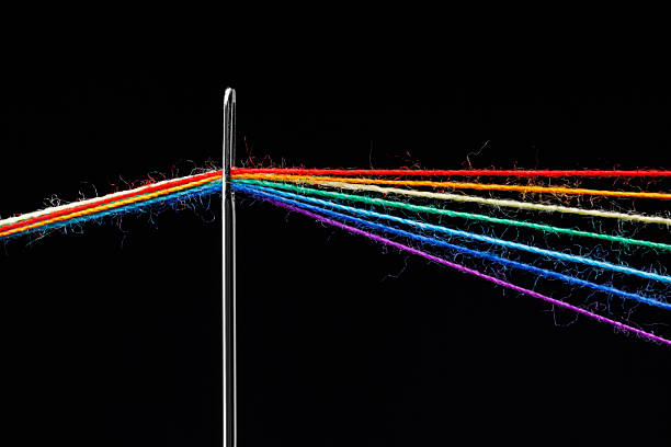 multi-colored threads for sewing in the form of a rainbow pass through an antique needle on a black background