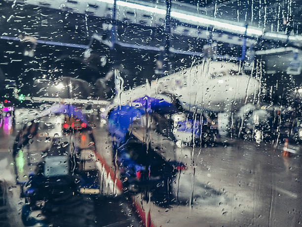 Moody, documentary-style image of a passenger jet parked at an airport gate, photographed from inside the terminal. The aircraft’s nose and cockpit windows are framed by the window mullions while a jet bridge is attached at the front door. The foreground glass is covered with condensation and vertical rain streaks, adding texture and conveying themes of waiting, delay, weather-affected travel, arrival and departure. Soft overcast light and a cool blue-gray palette create a calm, slightly somber atmosphere. The blurred, misted glass provides ample copy space for headlines or messages, making this a versatile background for stories on air travel, airline operations, business trips, passenger experience, flight cancellations, logistics, or sustainability in aviation. Shot in horizontal orientation; no people and no visible branding or logos are present, suitable for editorial use and conceptual commercial designs depending on agency policies.
