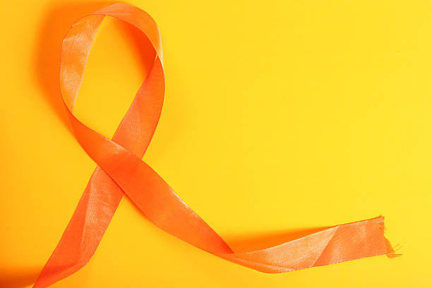 istock Orange awareness ribbon on a bright yellow background symbolizing support and hope. 2213246699