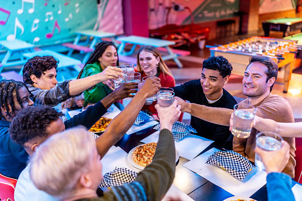 Young multiethnic friends toasting drinks at bowling alley restaurant