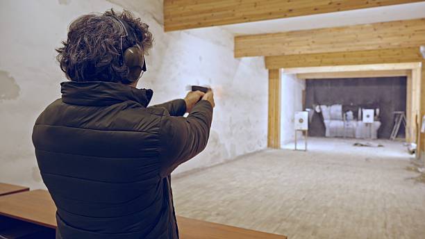 Male shooter shoots handgun at target inside shooting range. Mature man learning self devense and target sports. Training sports.