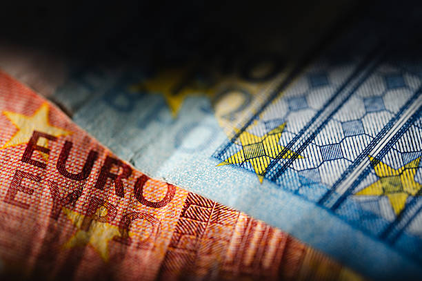 Close-up of overlapping 10 and 20 euro banknotes, emphasizing the detailed texture and color of the paper currency. Partially shadowed, the image combines precision printing with dramatic lighting, evoking themes of trust, economy, and financial depth.