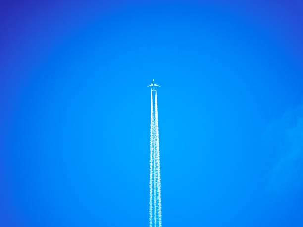 A high-altitude airplane flying through a clear blue sky, leaving two distinct contrails behind. The vibrant blue background emphasizes the sleek silhouette of the aircraft.