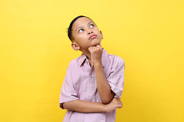 istock Thoughtful asian boy standing while looking up. Isolated on yellow background with copyspace 2213286002